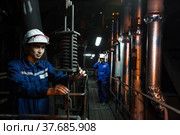 Ekibastuz, Pavlodar region, Kazakhstan - May 28, 2012: GRES-1 steam power station. Two workers in workshop. Dark background and gold-colored pipes. Left man with metal spring in focus. Стоковое фото, фотограф Alexey Rezvykh / Фотобанк Лори