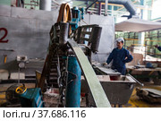 Pavlodar, Kazakhstan - May 29 2012: Rod production machine and worker operator in protective glass mask (right, blurred). Aluminium wire rod and cables workshop. Focus on rod. Редакционное фото, фотограф Alexey Rezvykh / Фотобанк Лори