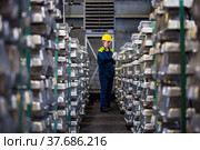Pavlodar, Kazakhstan - May 05 2012: Aluminium electrolysis plant. Ready ingots warehouse. Worker woman in yellow hardhat and blue workwear. Focus on ingots, worker blurred. Редакционное фото, фотограф Alexey Rezvykh / Фотобанк Лори