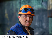 Aksu, Pavlodar region, Kazakhstan - May 29, 2012: Aksu steam power station. Portrait of adult Asian worker in orange hardhat. With welding protective glasses. Close up photo. Blurred background. Редакционное фото, фотограф Alexey Rezvykh / Фотобанк Лори