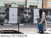 Москва. Люди рассматривают фотовыставку "Дети Донбасса" на улице Арбат (2022 год). Редакционное фото, фотограф Дмитрий Неумоин / Фотобанк Лори