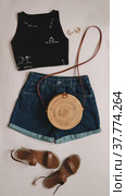 flat lay composition with female top, denim shorts, sandals and a wicker rattan bag on beige background top view. Стоковое фото, фотограф Galina kondratenko / Фотобанк Лори