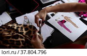 A female designer draws examples of clothes in a sketchbook and cuts out pieces of leopard cloth. Стоковое видео, видеограф Константин Шишкин / Фотобанк Лори