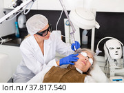 Focused cosmetologist performing laser resurfacing to senior woman. Стоковое фото, фотограф Яков Филимонов / Фотобанк Лори
