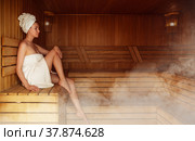 Young woman relaxing and sweating in hot sauna wrapped in towel. Girl In Sauna. Interior of Finnish sauna, classic wooden sauna with hot steam. Russian bathroom. Relax in hot sauna with steam. Стоковое фото, фотограф Сергей Тимофеев / Фотобанк Лори