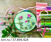 The process of hand embroidery with satin ribbons on green canvas of pink three-leaf clover flowers  and sets of colored ribbons on wooden background. Handmade gift for St. Patrick's Day (embroidery made the author of photo) Стоковое фото, фотограф Виктория Катьянова / Фотобанк Лори
