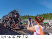 Туристы на железнодорожной станции «Горный парк Рускеала» фотографируют ретропоезд на паровозной тяге «Рускеальский экспресс» (2022 год). Редакционное фото, фотограф Румянцева Наталия / Фотобанк Лори