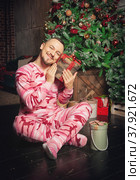 Cheerful funny man in pink sleepwear near decorated fir tree and hold Christmas present. Стоковое фото, фотограф Darkbird77 / Фотобанк Лори