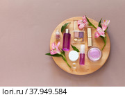 Top view on natural decorative cosmetics with flower extracts on wooden round podium at beige background. Advertising new cosmetic products. Anti-aging skin care. Flat lay, copy space, mock up. Стоковое фото, фотограф Виктория Катьянова / Фотобанк Лори