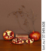 Beautiful still life with ripe pomegranates and a rhodonite stone box on wooden table. Can be used as a podium for the presentation of cosmetics with fruit extracts. Front view, brown background, mock up. Стоковое фото, фотограф Виктория Катьянова / Фотобанк Лори