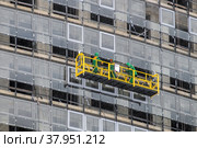 Minsk, Belarus - December 01, 2018: Workers in a construction cradle at a height are engaged in glazing the facade of a skyscraper in winter. Side view. Редакционное фото, фотограф Denis Shitikoff / Фотобанк Лори