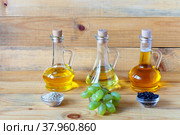 Three types of healthy vegetable oils: sesame, grapeseed and sunflower, in glass jugs and plant seeds on a wooden background. Healthy foods with vitamins E and A. Стоковое фото, фотограф Виктория Катьянова / Фотобанк Лори