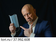 Мужчина держит в руке медицинскую маску. Демонстрация средств защиты органов дыхания. Стоковое фото, фотограф Виталий Михайлюк / Фотобанк Лори