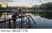Мужчина любуется вечерним городским пейзажем возле озера. Лысый парень в спортивной одежде стоит на пирсе реки, облокотившись на поручни. Отдых в городском общественном парке. Красивое отражение на водной глади. Привлекательный мужчина. Man admires evening cityscape near lake. Bald guy in sports clothes standing on pier of river, leaning on handrails. Recreation in city public park. Beautiful reflection on water surface. Handsome man. Стоковое видео, видеограф Ирина / Фотобанк Лори