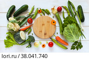 Fresh organic vegetables lie on table around cutting board before preparing vitamin summer meal. Freshly picked: carrot, cucumber, cauliflower, zucchini, tomato, peas, beans, broccoli and cabbage. Стоковое фото, фотограф Виктория Катьянова / Фотобанк Лори