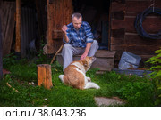 Russia Polevskoy August 2021: An elderly man relaxes near a Russian bathhouse with his dog and smokes a cigarette. Редакционное фото, фотограф Акиньшин Владимир / Фотобанк Лори