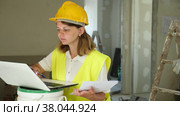 Female foreman in a protective helmet and a yellow vest checks the execution of repair work using a laptop. Стоковое видео, видеограф Яков Филимонов / Фотобанк Лори