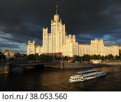 Высотное здание на Котельнической набережной. В лучах закатного солнца на фоне темных облаков с идущем кораблем на переднем фоне (2022 год). Редакционное фото, фотограф SevenOne / Фотобанк Лори