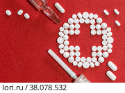 Композиция из лекарственных таблеток, шприца и ампулы на поверхности красной искусственной кожи. Макет для рецепта. Стоковое фото, фотограф Борис Ряузов / Фотобанк Лори