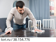 Young bachelor wiping surface of dining table in apartment. Стоковое фото, фотограф Яков Филимонов / Фотобанк Лори