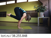 Женщина в спортивной одежде практикующая йогу, выполняет упражнение бакасана, поза журавля, балансовая асана, тренируется на коврике в студии. Стоковое фото, фотограф Сергей Чайко / Фотобанк Лори