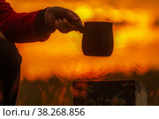beautiful mature woman brews coffee in a turk in the oven in nature against the backdrop of dawn. Стоковое фото, фотограф Акиньшин Владимир / Фотобанк Лори