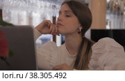 Girl Slavic appearance in white jacket in evening sits at table in bar with laptop. Стоковое видео, видеограф Aleksandr Golubev / Фотобанк Лори