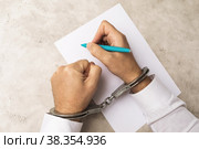 Человек в наручниках пишет завещание или признание в преступлении, концепция получения согласия под влиянием давления на людей. Стоковое фото, фотограф Сергей Чайко / Фотобанк Лори