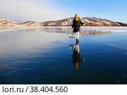 A happy girl looks at her reflection on the ice of the frozen Lake Baikal. He holds skates in his hands. Стоковое фото, фотограф Виктория Тельминова / Фотобанк Лори
