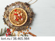 Christmas porridge with nuts and candied fruits. In the center of the wreath of cones and fir branches. On a light wooden background with space. Стоковое фото, фотограф Bogdanova Mariia / Фотобанк Лори