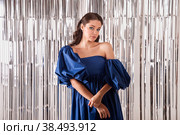 Elegant vogue woman model in blue dress at bright tinsel background celebrating festive holiday, looking at camera. Beautiful positive charming lady posing on glittered backdrop. Copy text space. Стоковое фото, фотограф Aleksandr Golubev / Фотобанк Лори