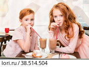 Two little sobs-haired girls at a table in cafe drink through a tube of cocoa. Стоковое фото, фотограф Мария Мороз / Фотобанк Лори