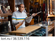 Hispanic salesman showing collectible rifled musket in gun store. Стоковое фото, фотограф Яков Филимонов / Фотобанк Лори
