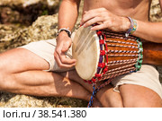 Close up hands young man drummer, playing rhythm with djembe drum, sitting at tropical coral reef coast background. Travel vacation and music relaxation concept. Selective focus. Copy text space. Стоковое фото, фотограф Aleksandr Golubev / Фотобанк Лори
