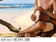 Close up hands young man drummer, playing rhythm on djembe drum on tropical sandy beach at ocean background. Travel vacation and music relaxation concept. Selective focus. Copy text space. Стоковое фото, фотограф Aleksandr Golubev / Фотобанк Лори