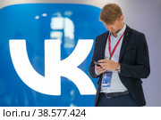 Россия. Санкт-Петербург. Молодые люди со смартфоном на фоне логотипа социальной сети ВКонтакте. Russia. Saint-Petersburg. Young people with a smartphone on the background of the VKontakte social network logo. (2022 год). Редакционное фото, фотограф Алексей Смышляев / Фотобанк Лори