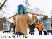 Россия. Ленинградская область, Тайцы. Празднование праздника Масленица. народные гуляния на Масленицу. Девушка несет ведра на коромысле. Russia. Leningrad region, Thais. Celebration of the Maslenitsa holiday. folk festivals on Maslenitsa. The girl carries buckets on a yoke. (2021 год). Редакционное фото, фотограф Алексей Смышляев / Фотобанк Лори