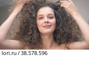 Close-up of a beautiful young woman with curly hair, she tilts her head in different directions, smiling at the camera, touching her hair with her hands. Стоковое видео, видеограф Darya Komarova / Фотобанк Лори