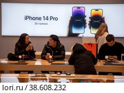 Покупатели выбирают гаджеты компании Apple на фоне рекламы телефона Iphone 13 Pro в магазине ЦУМ в центре города Москвы, Россия (2023 год). Редакционное фото, фотограф Николай Винокуров / Фотобанк Лори