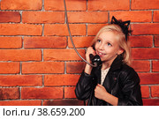 Portrait little girl model in leather jacket calling old payphone at brick wall background, smiling. Child emotional lady talking telephone outdoor. Communication lifestyle concept. Copy text space. Стоковое фото, фотограф Aleksandr Golubev / Фотобанк Лори