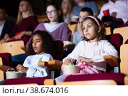 Preteen girl with mulatta mate watching movie in cinema. Стоковое фото, фотограф Яков Филимонов / Фотобанк Лори