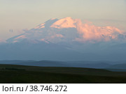 Great nature mountain range. Amazing perspective of snow mountain or volcano Elbrus at sunset with clouds, green fields, blue sky background. Elbrus landscape view - highest peak of Russia and Europe. Стоковое фото, фотограф Евгений / Фотобанк Лори
