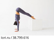Женщина в спортивной одежде выполняет вариацию упражнения адхо мукха врикшасана, перевернутая асана дерева, стоит на руках и опирается ногами на куб на светлом фоне. Стоковое фото, фотограф Сергей Чайко / Фотобанк Лори