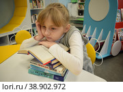 Девочка школьница 8 лет со стопкой книг подпирает щеку рукой. Библиотека нового поколения (2022 год). Редакционное фото, фотограф Наталья Зверева / Фотобанк Лори
