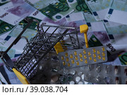 medicines and pills are lying in a small shopping cart against the background of money euro dollars 100 500. pills are poured out of the cart for money the problem of the cost of medicines expensive m. Стоковое фото, фотограф Meshkov Sergey / Фотобанк Лори