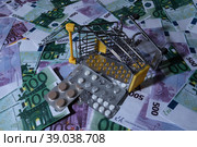 medicines and pills are lying in a small shopping cart against the background of money euro dollars 100 500. pills are poured out of the cart for money the problem of the cost of medicines expensive m. Стоковое фото, фотограф Meshkov Sergey / Фотобанк Лори