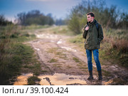 Молодой мужчина турист с рюкзаком идет по размытой грязной дороге на фоне вечернего заката. Стоковое фото, фотограф Мария Мороз / Фотобанк Лори