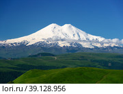 Nature mountain range. Amazing perspective of caucasian snow mountain or sleeping volcano Elbrus with green fields, blue sky background. White Elbrus landscape view - highest peak of Russia and Europe. Стоковое фото, фотограф Евгений / Фотобанк Лори