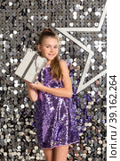 Cover girl in disco dress with gift box posing at bright background with star, looking at camera. Pretty party girl with hairstyle in silver wear. Retro discotheque concept. Copy text space for ad. Стоковое фото, фотограф Aleksandr Golubev / Фотобанк Лори