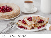 Russian traditions. Russian holiday Maslenitsa. Still life with a cup of tea, a stack of pancakes with northern cranberries, cubes of butter on the table. Стоковое фото, фотограф Photojuli / Фотобанк Лори